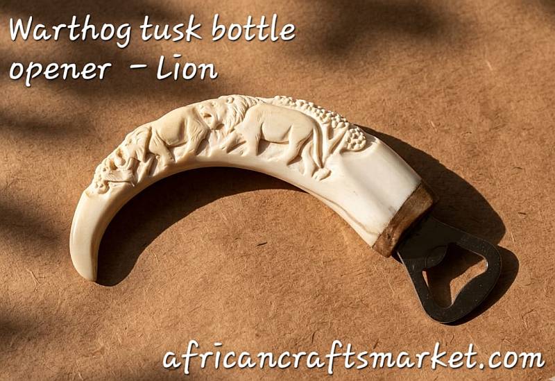 A genuine African warthog tusk bottle opener featuring a highly detailed, hand-carved 3D relief sculpture of a male lion head with a full mane on the polished ivory handle