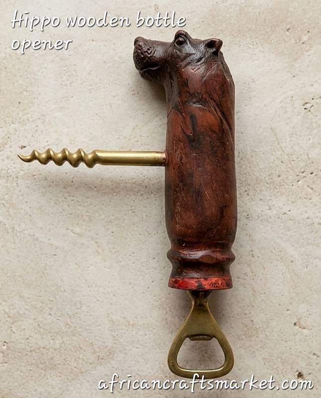 A handcrafted African wooden bottle opener carved into the smooth, heavy shape of a hippopotamus, featuring a durable metal opener mechanism integrated into the base